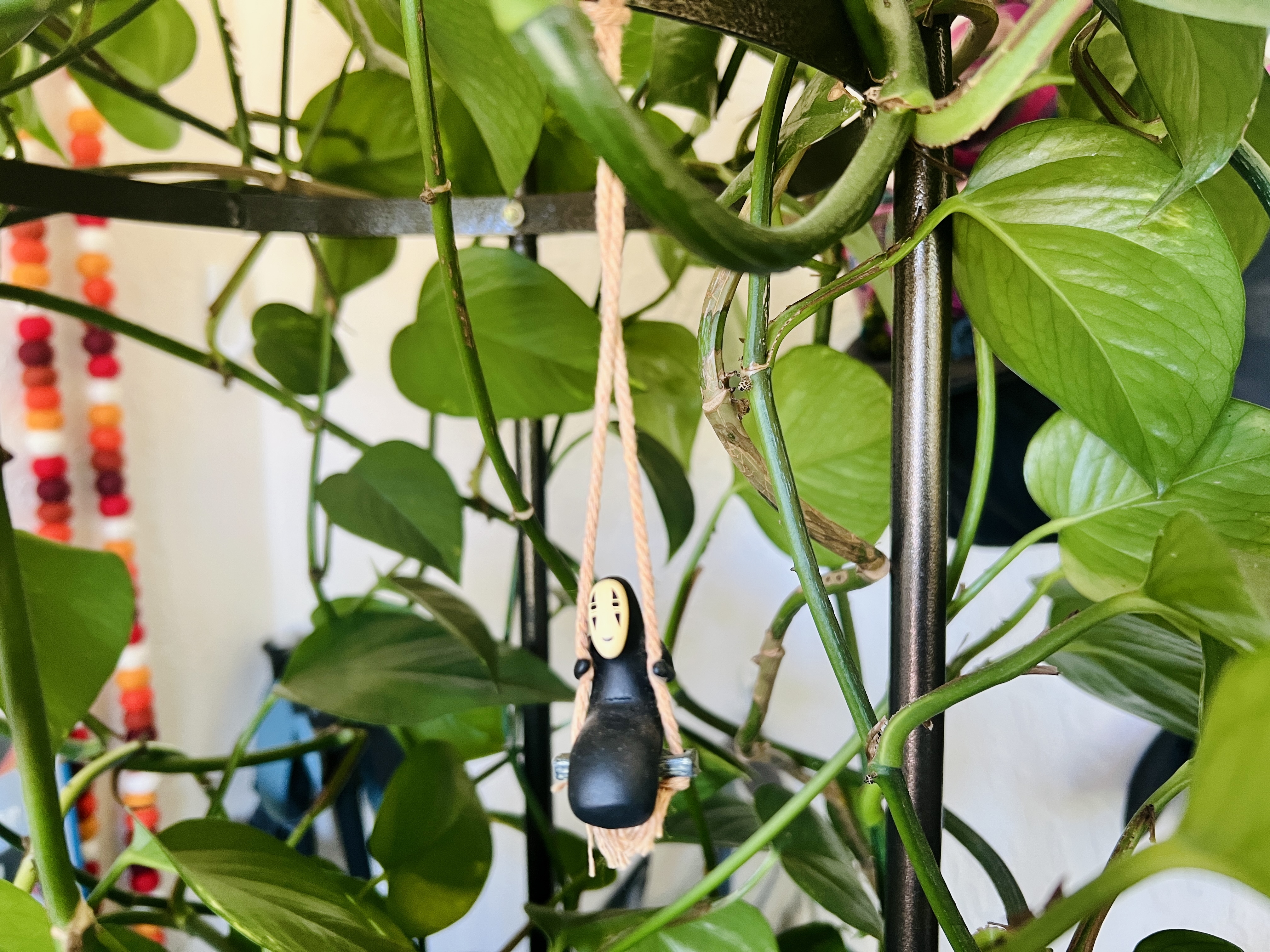 A tiny figurine of the character No-Face from Spirited Away, he's swinging in a little swing